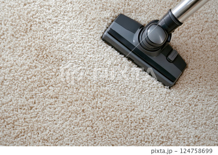 Overhead close-up of a black vacuum cleaner head moving across a fluffy beige carpet 124758699