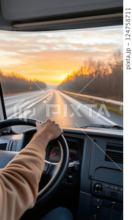 Over-the-shoulder view of a truck driver holding the steering wheel while driving on a highway at sunset 124758711