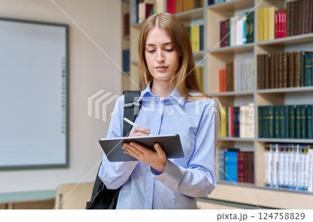 Portrait of student teenager girl using digital tablet inside classroom library 124758829
