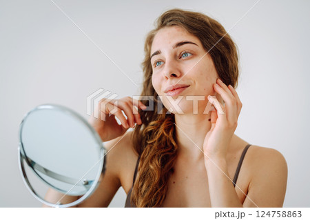 Beautiful woman with problematic skin looks in her small mirror. Cosmetology. Skin care concept. Beautiful woman with problematic skin looks in her small mirror. Cosmetology. Skin care concept. 124758863