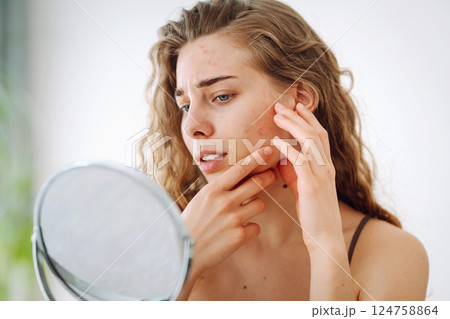 Beautiful woman with problematic skin looks in her small mirror. Cosmetology. Skin care concept. 124758864