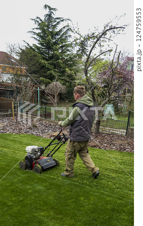 Nitra, Slovakia - 04.02.2025: Man trims the grass with a trimmer on the lawn. Mowing the lawn. 124759553