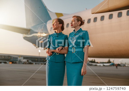 Stylish Flight Attendants Posing Gracefully by their Airplane during a Beautiful Sunset 124759740