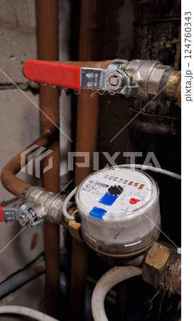 Close-up of residential water meter with red valve handles on copper pipes 124760343