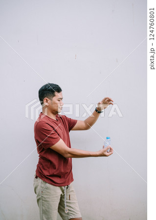 Man in Casual Attire Holding a Water Bottle Against Plain Background 124760801
