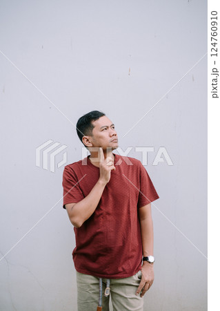 Man in maroon thinking deeply against a neutral backdrop pondering 124760910