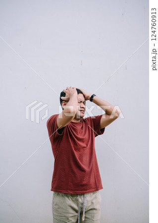 Man holding his head in distress against a plain background Man holding his head in distress against a plain background 124760913