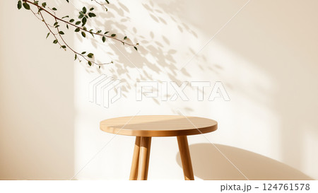A simple wooden table with a round top filled with a coating that provides sunlight. The delicate shadows of leafy branches play on the textured cream wall in the background. 124761578