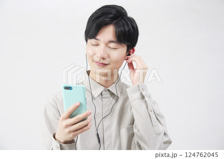 イヤホンをつけて音楽を聴く20代男性 白背景 イヤホンをつけて音楽を聴く20代男性 白背景 124762045