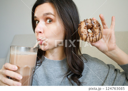 Funny girl drinking cacao from a big glass with cappuccino donut Funny girl drinking cacao from a big glass with cappuccino donut 124763085