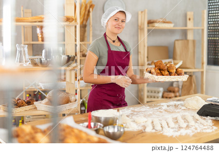Young woman baker are standing near product range in bakery kitchen with basket of croissants. 124764488