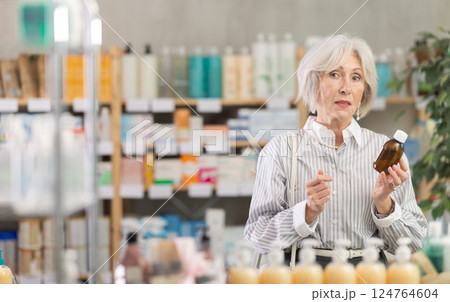 Elderly woman chooses syrup at pharmacy 124764604