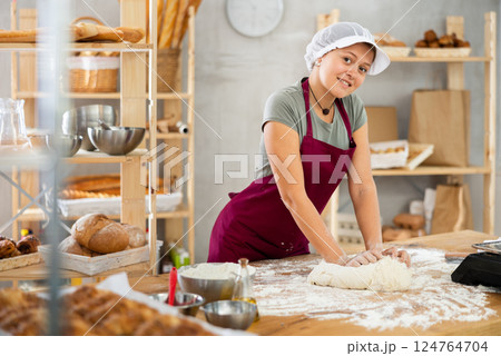 Working in bakery - girl kneads raw dough to make baguettes or croissants 124764704