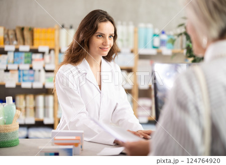 Woman employee at counter with computer sells pills and ointments to customer Woman employee at counter with computer sells pills and ointments to customer 124764920