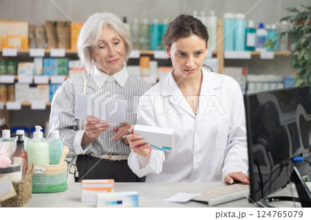 Female pharmacist with a package of pills working at a computer in front of a client 124765079