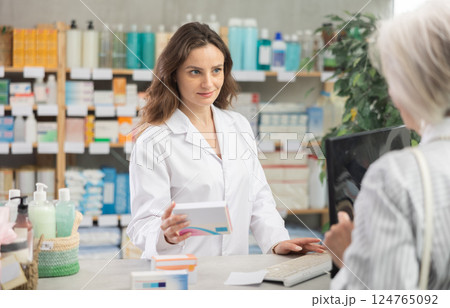 female pharmacist advises a client behind the counter in a pharmacy 124765092