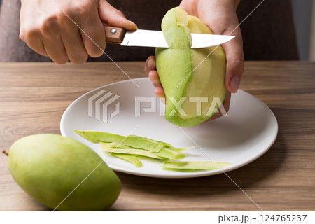Hand holding kitchen knife and peeling green mango to making salad Hand holding kitchen knife and peeling green mango to making salad 124765237
