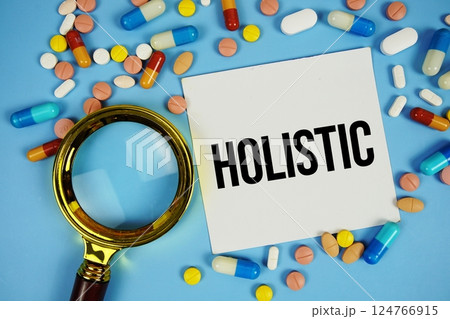 Holistic text on sticky note paper with Medicine and Magnifying glass on blue background Holistic text on sticky note paper with Medicine and Magnifying glass on blue background 124766915