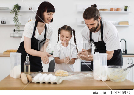 Smiling young parents and daughter in kitchen making dough, sharing happy bonding moment together 124766977