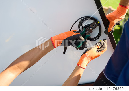 Worker building solar panel system on metal rooftop of house. Man technician preparing to install photovoltaic solar module outdoors. Alternative, green and renewable energy generation concept. Worker building solar panel system on metal rooftop of house. Man technician preparing to install photovoltaic solar module outdoors. Alternative, green and renewable energy generation concept. 124768664