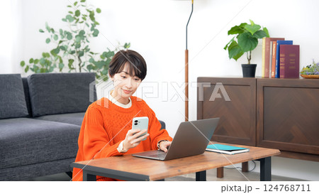 リビングルームでスマホとノートパソコンを使うミドル女性 リビングルームでスマホとノートパソコンを使うミドル女性 124768711