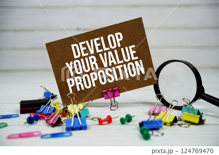 Develop Your Value Proposition text on paper card with magnifying glass and stationary on wooden background Develop Your Value Proposition text on paper card with magnifying glass and stationary on wooden background 124769470