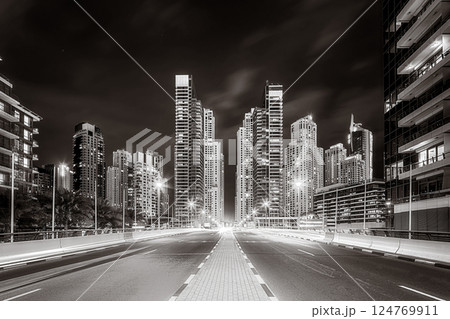 Urban city skyline with illuminated skyscrapers and waterfront railing in black and white at night, Dubai Marina bay UAE 124769911