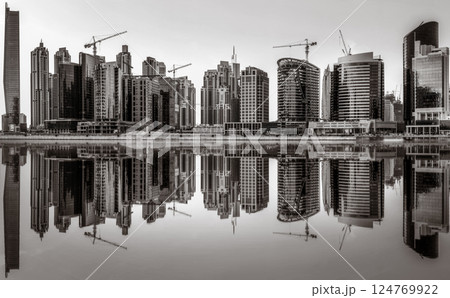 Monochrome city skyline with tall skyscrapers reflecting on calm water under a cloudy sky, Dubai Marina bay UAE Monochrome city skyline with tall skyscrapers reflecting on calm water under a cloudy sky, Dubai Marina bay UAE 124769922