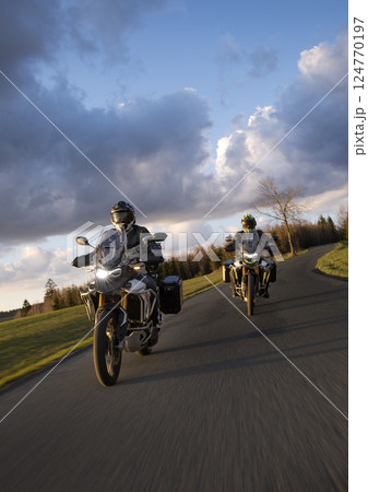 Drivers riding motorcycle on empty road during sunset, spring mountains 124770197