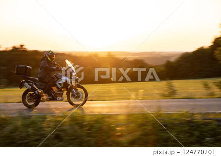Driver riding motorcycle on empty road during sunset, spring mountains Driver riding motorcycle on empty road during sunset, spring mountains 124770201
