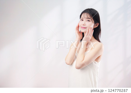 笑顔でお肌のケアをする若い女性（シンプル背景） 124770287