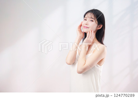 笑顔でお肌のケアをする若い女性（シンプル背景） 124770289