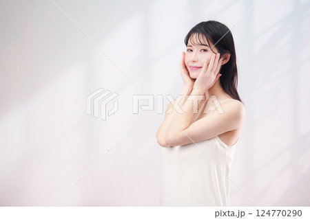 笑顔でお肌のケアをする若い女性(シンプル背景) 笑顔でお肌のケアをする若い女性(シンプル背景) 124770290