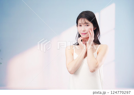 笑顔でお肌のケアをする若い女性(シンプル背景) 笑顔でお肌のケアをする若い女性(シンプル背景) 124770297