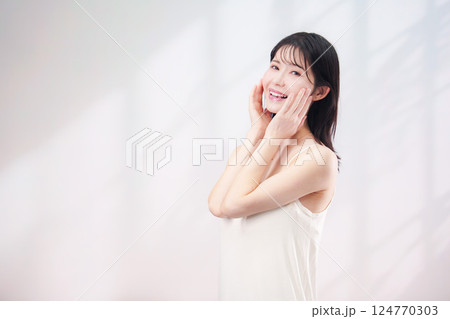 笑顔でお肌のケアをする若い女性(シンプル背景) 笑顔でお肌のケアをする若い女性(シンプル背景) 124770303