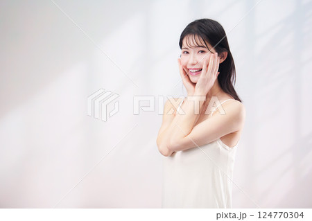 笑顔でお肌のケアをする若い女性（シンプル背景） 124770304