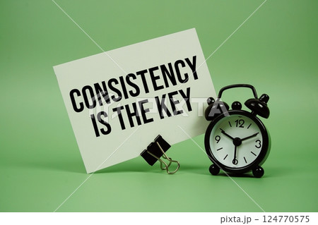 Consistency Is The Key text message on paper card with alarm clock on green background Consistency Is The Key text message on paper card with alarm clock on green background 124770575