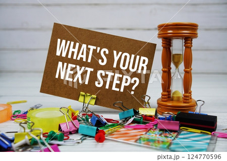 What's Your Next Step? text on paper card with alarm clock and stationary on wooden background 124770596