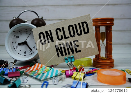 On Cloud Nine text on paper card with alarm clock and stationary on wooden background On Cloud Nine text on paper card with alarm clock and stationary on wooden background 124770613