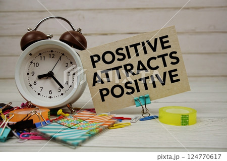 Positive Attracts Positive text on paper card with alarm clock and stationary on wooden background 124770617
