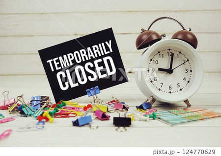 Temporarily Closed text on paper card with alarm clock and stationary on wooden background 124770629