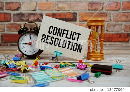 Conflict Resolution text on paper card with alarm clock and stationary on wooden background Conflict Resolution text on paper card with alarm clock and stationary on wooden background 124770644
