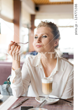 A woman is sitting at a table with a cup of coffee and a spoon 124771386