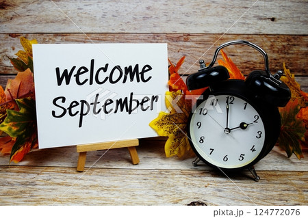 Welcome September text with alarm clock and maple leaf decoration on wooden background 124772076
