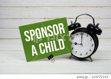 Sponsor A Child text message on paper card with alarm clock on wooden background 124772143