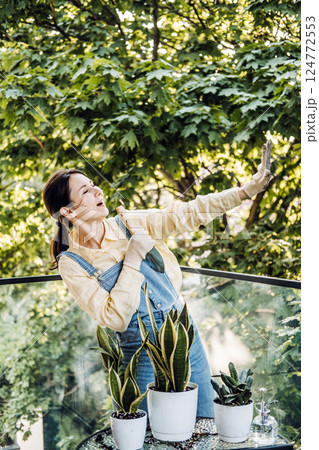 Young Asian woman playfully singing into a garden trowel while caring for balcony plants. Plant therapy, Gen Z self-expression, emotional wellness, sustainable hobbies Young Asian woman playfully singing into a garden trowel while caring for balcony plants. Plant therapy, Gen Z self-expression, emotional wellness, sustainable hobbies 124772553