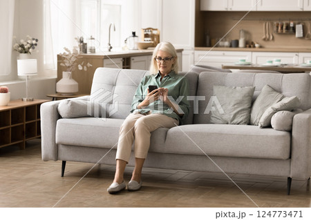 Old age woman rest on cozy couch texting on phone 124773471