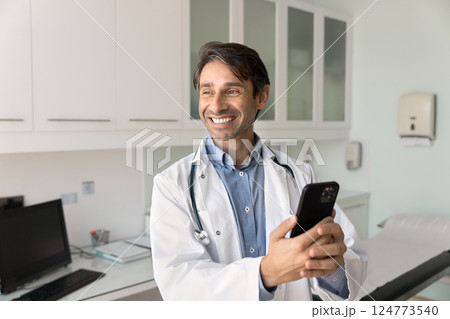 Happy male doctor using phone in workplace Happy male doctor using phone in workplace 124773540
