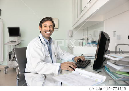 Happy male professional doctor sits at desk working on pc 124773546