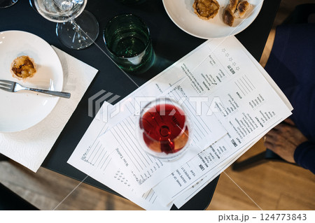 Close-up of wine tasting session with red wine glass, printed tasting notes, and appetizers on a dark table. Wine workshop, hands-on wine education, tasting notes analysis, sommelier training Close-up of wine tasting session with red wine glass, printed tasting notes, and appetizers on a dark table. Wine workshop, hands-on wine education, tasting notes analysis, sommelier training 124773843
